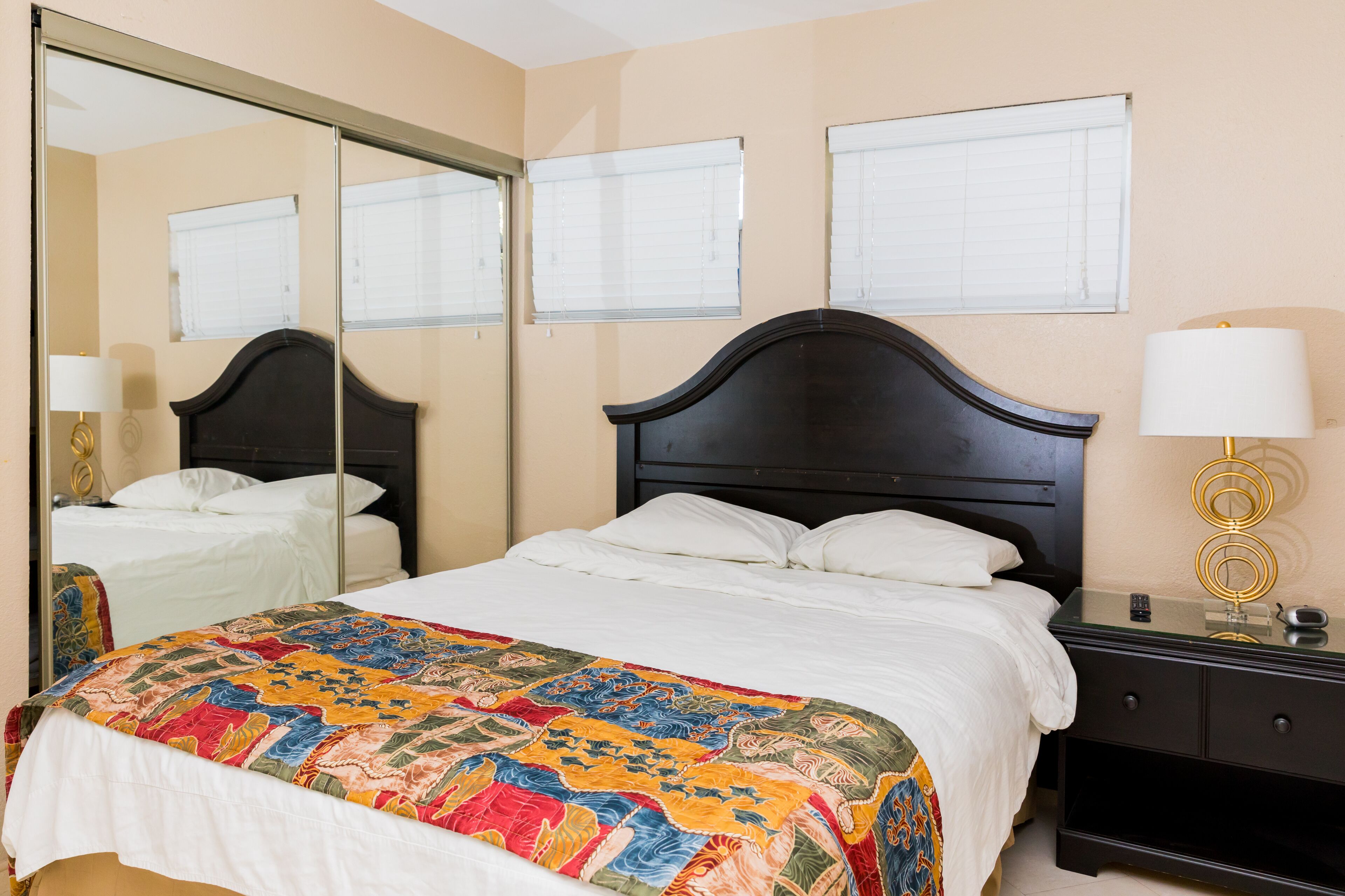 A bedroom with a large bed, a dresser, a nightstand, and a mirror.