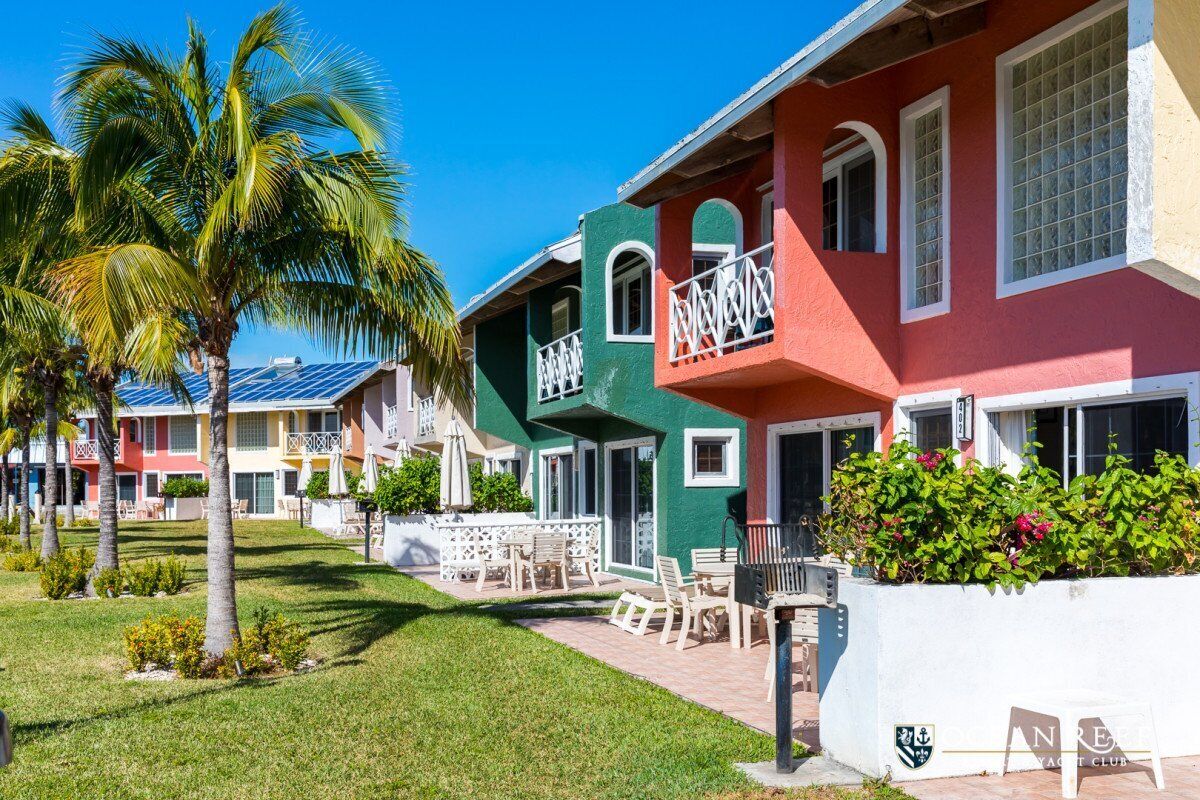 A row of colorful buildings with balconies, a palm tree, and a well-maintained lawn.