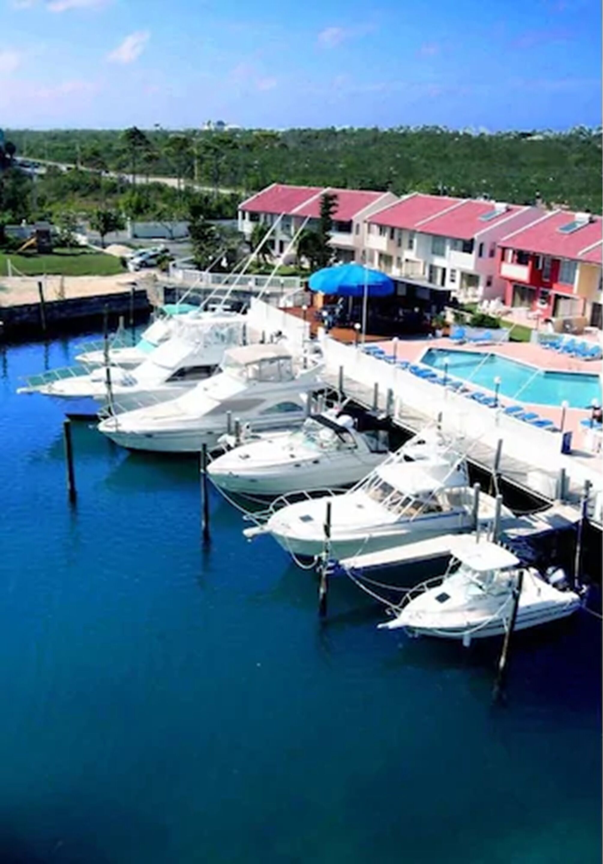 Uma marina com vários barcos atracados, uma piscina e uma fileira de edifícios com telhados vermelhos.