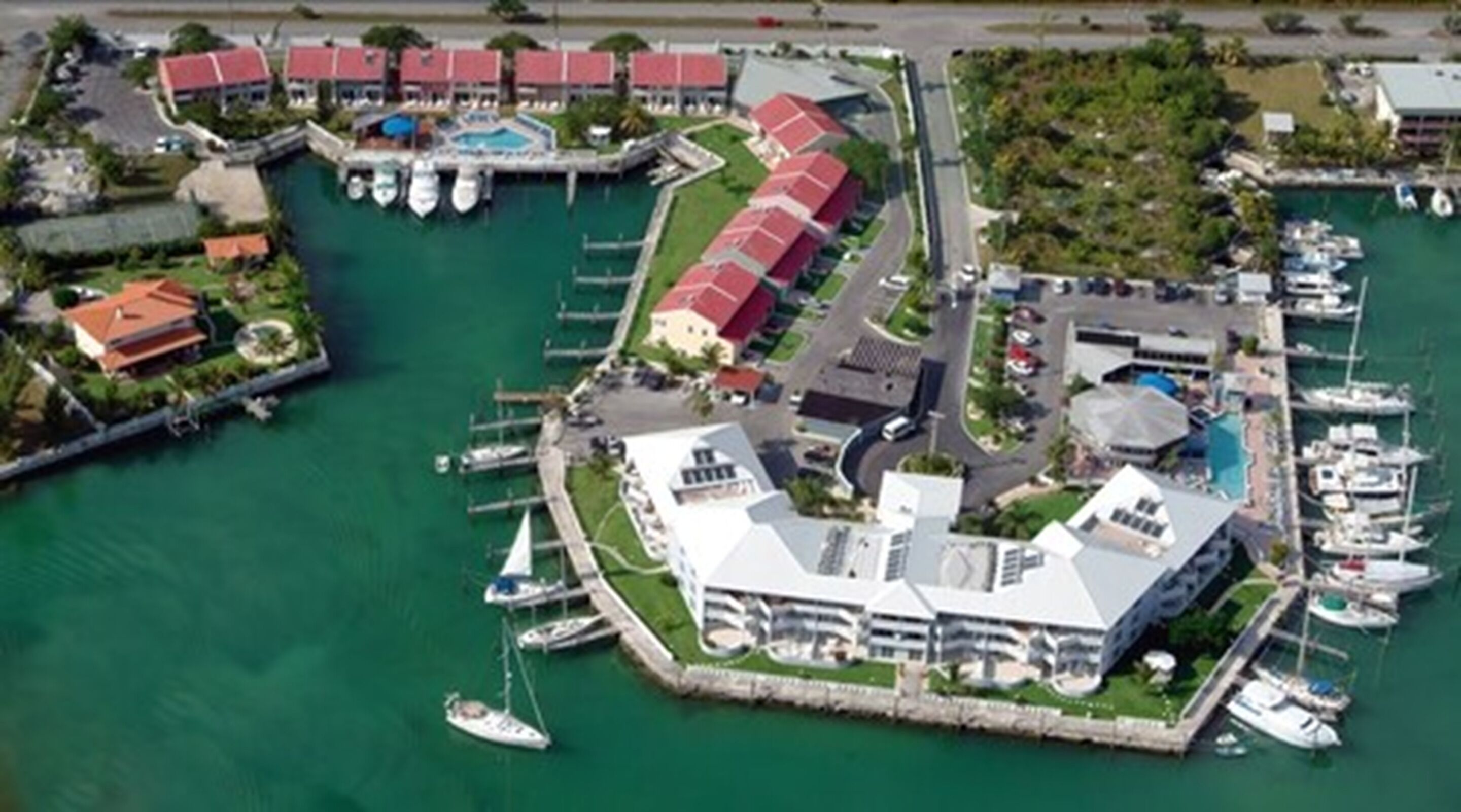 An aerial view of a marina with multiple docks, boats, and a large building with a distinctive roof.