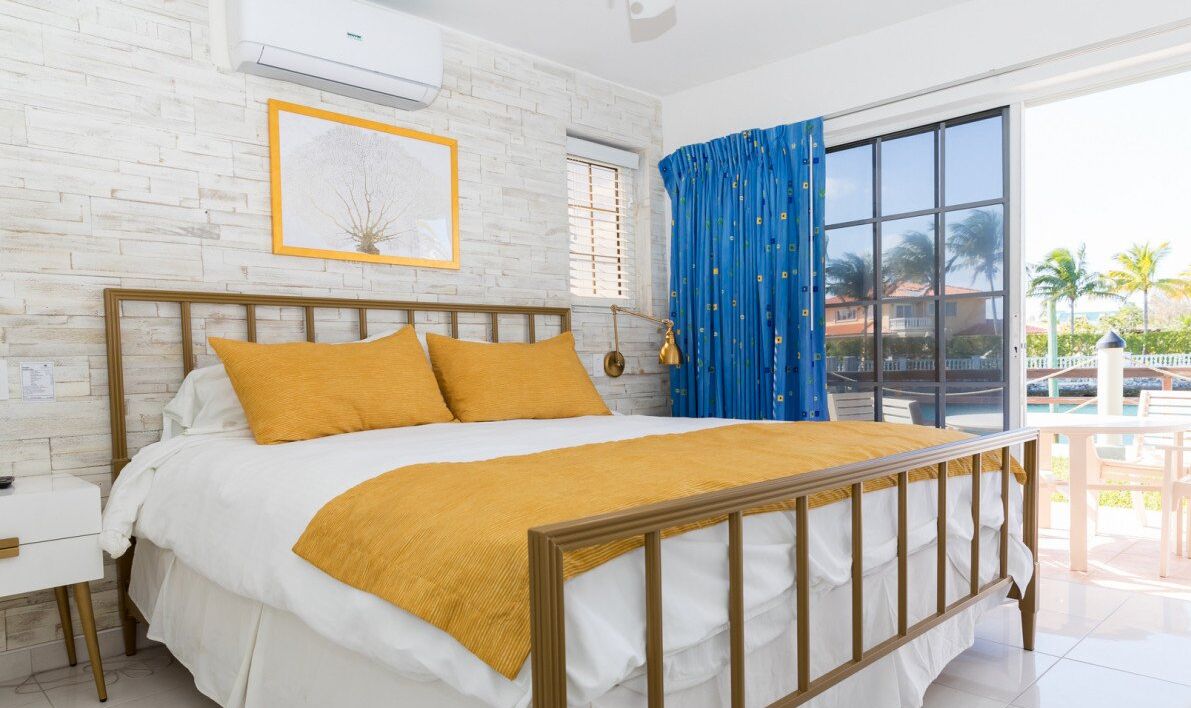 Un dormitorio con cama de madera, ropa de cama blanca, una cortina azul y vistas al exterior.