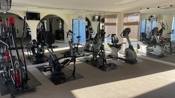 A gym with various exercise equipment, including stationary bikes and treadmills, arranged in a spacious layout with large windows allowing natural light.