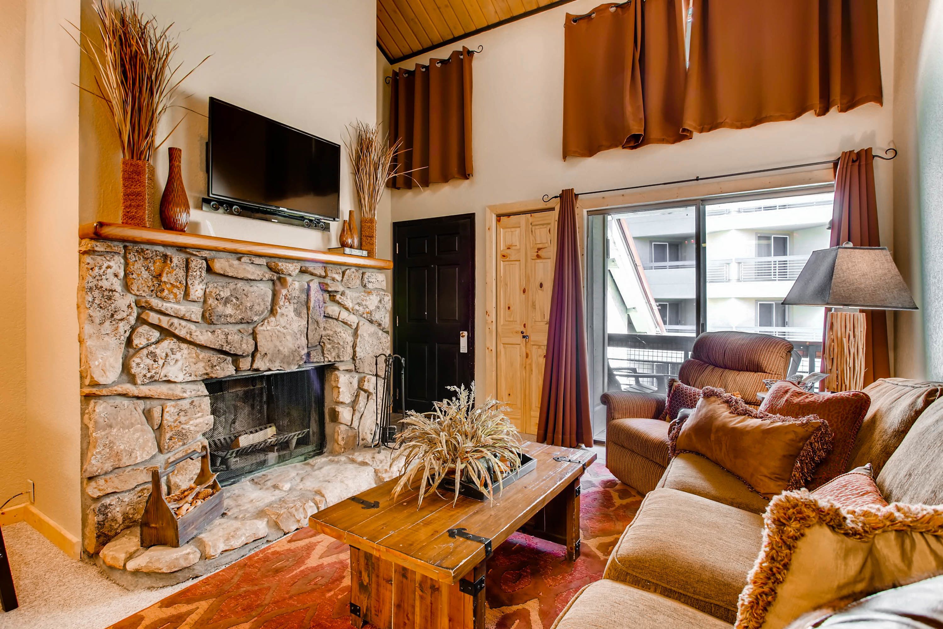 A cozy living room with a stone fireplace, a flat-screen TV, a wooden coffee table, and a comfortable sofa.