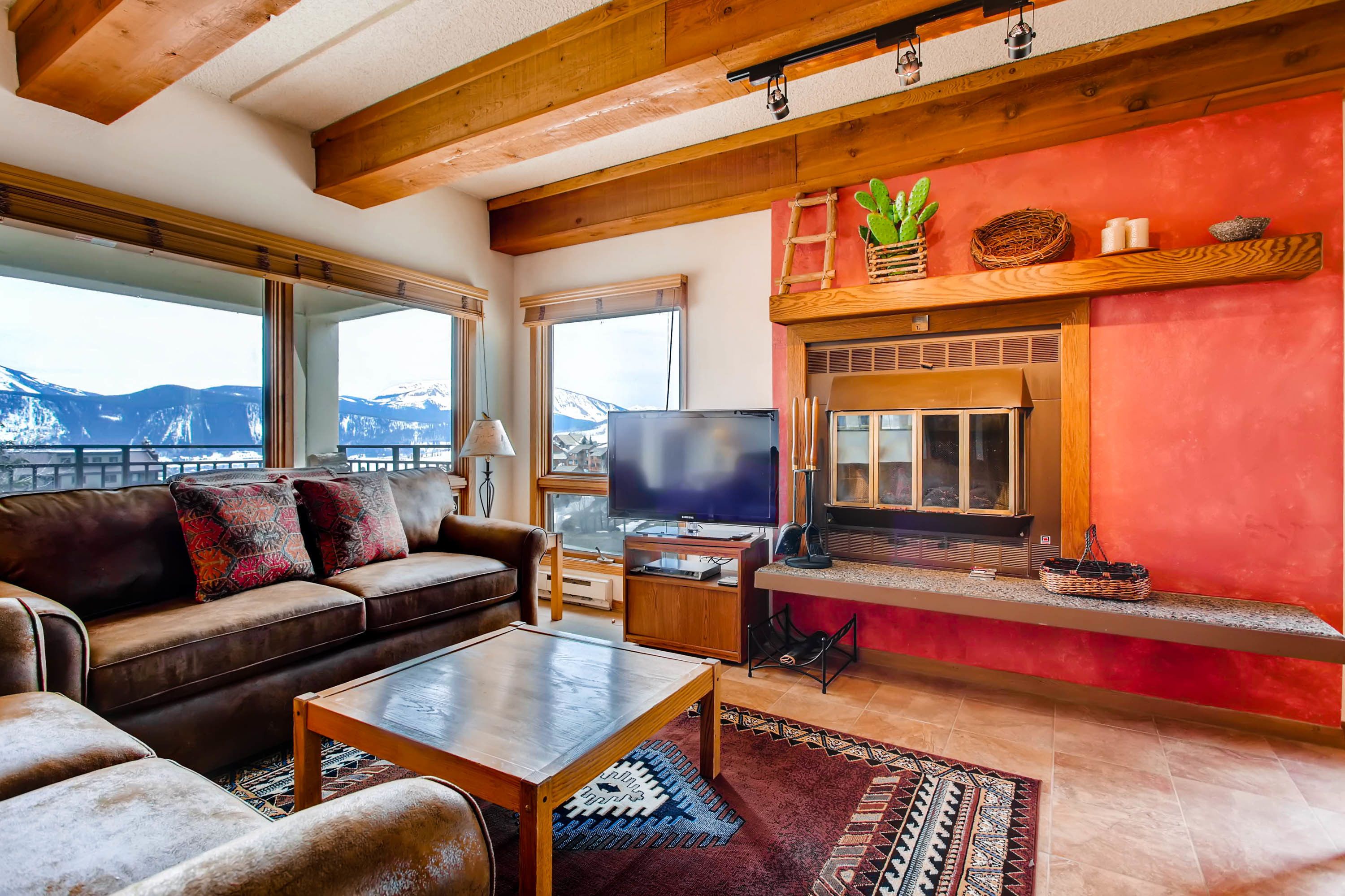 Una sala de estar acogedora con un sofá de cuero, un televisor de pantalla plana, una chimenea y vistas a montañas a través de amplias ventanas.