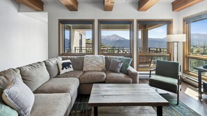 A modern living room with a sectional sofa, a wooden coffee table, and large windows offering a mountain view.