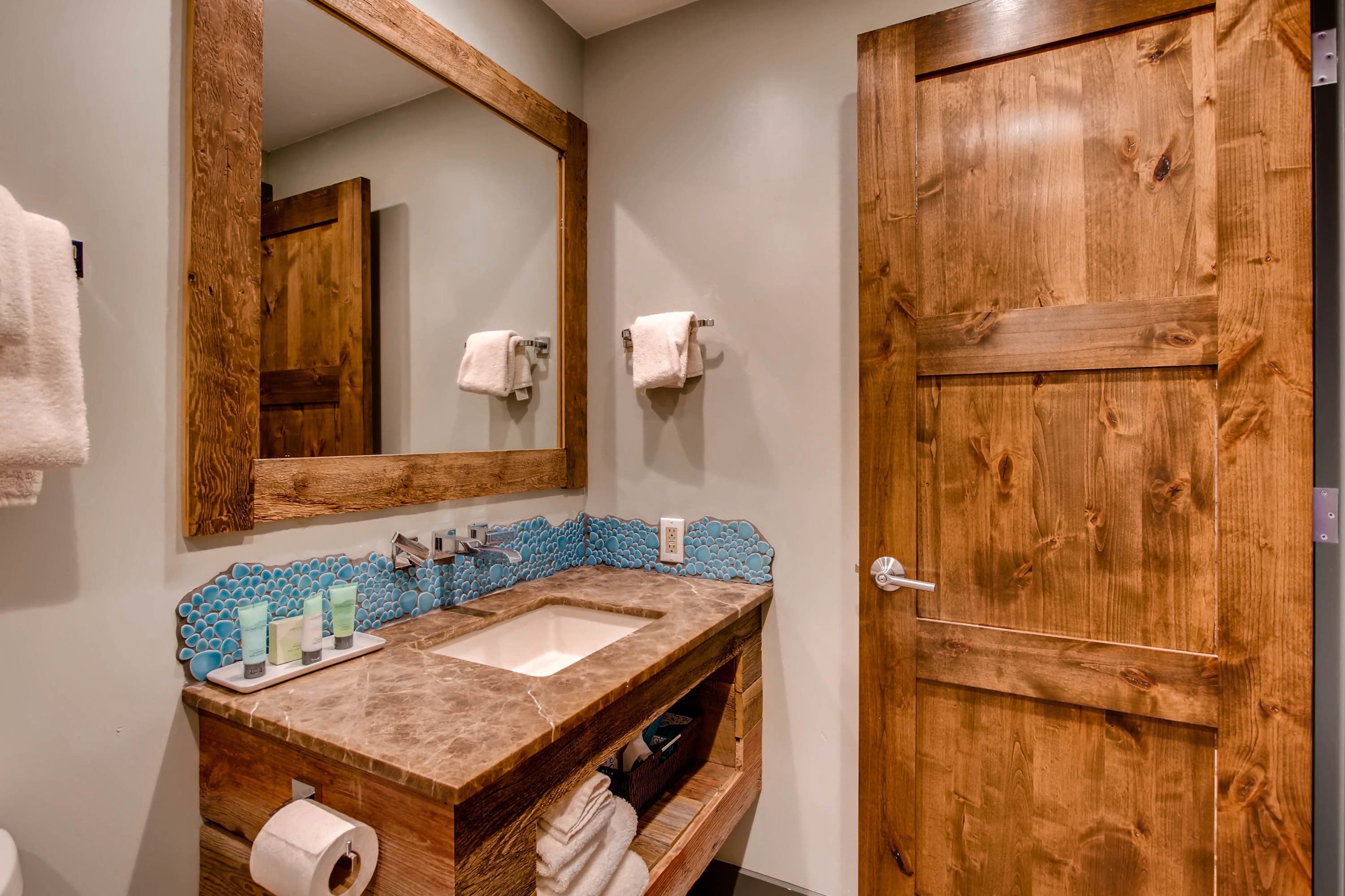 A bathroom with a wooden vanity, a large mirror, and a wooden door.