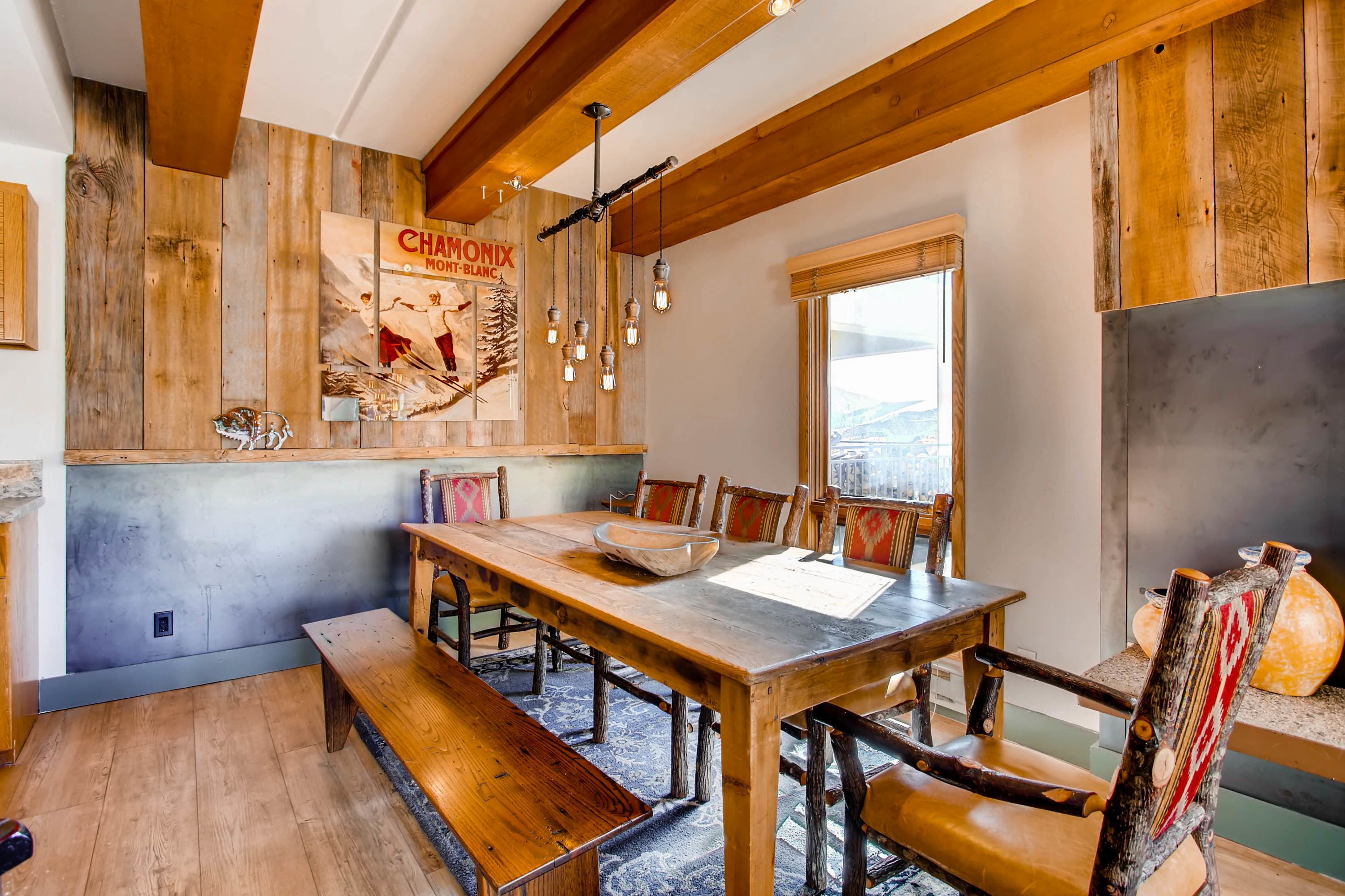 A rustic dining area with wooden furniture, a large table, benches, and a hanging light fixture.