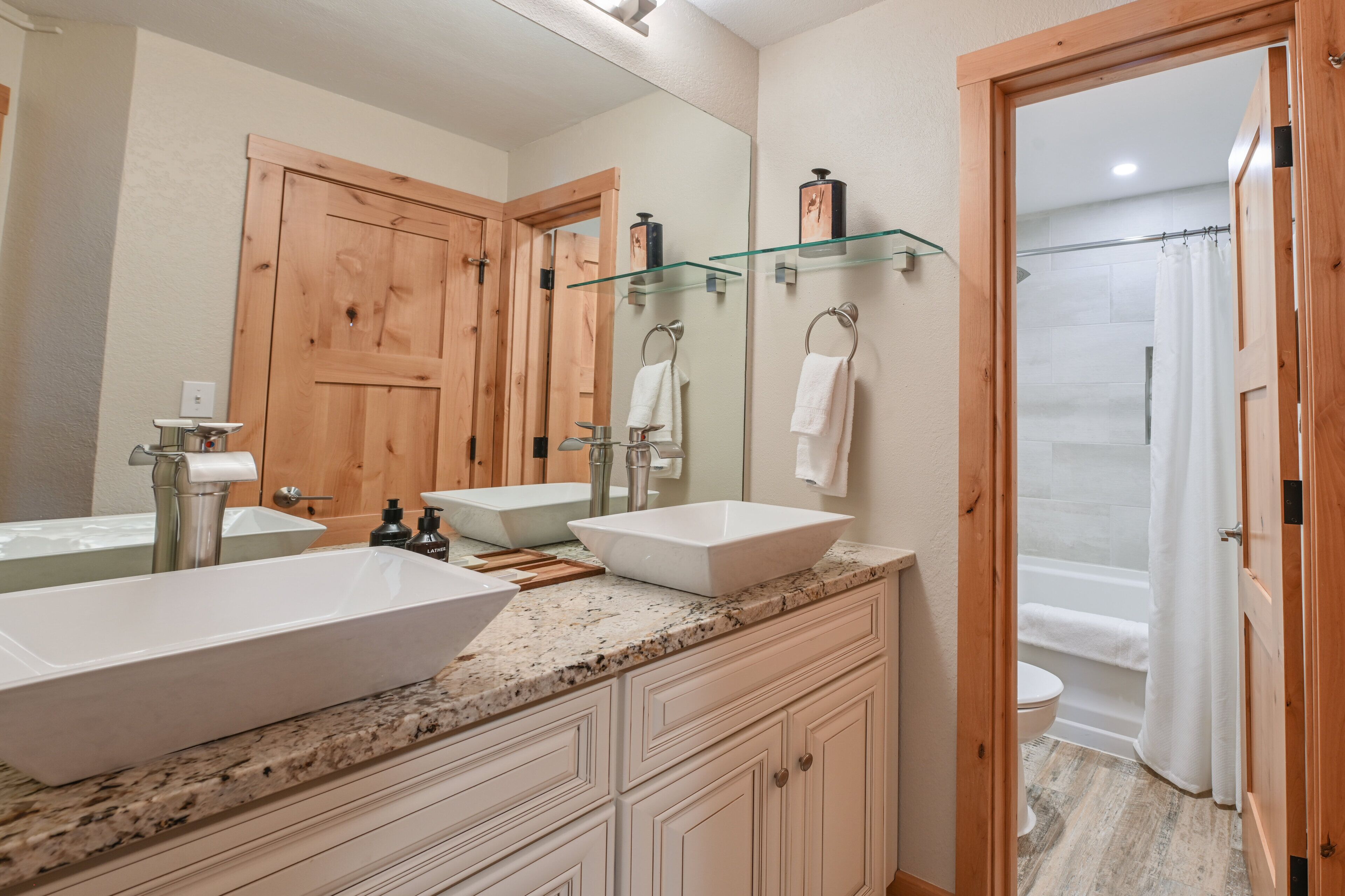 Une salle de bain avec deux lavabos, un grand miroir, des portes en bois et un espace douche.