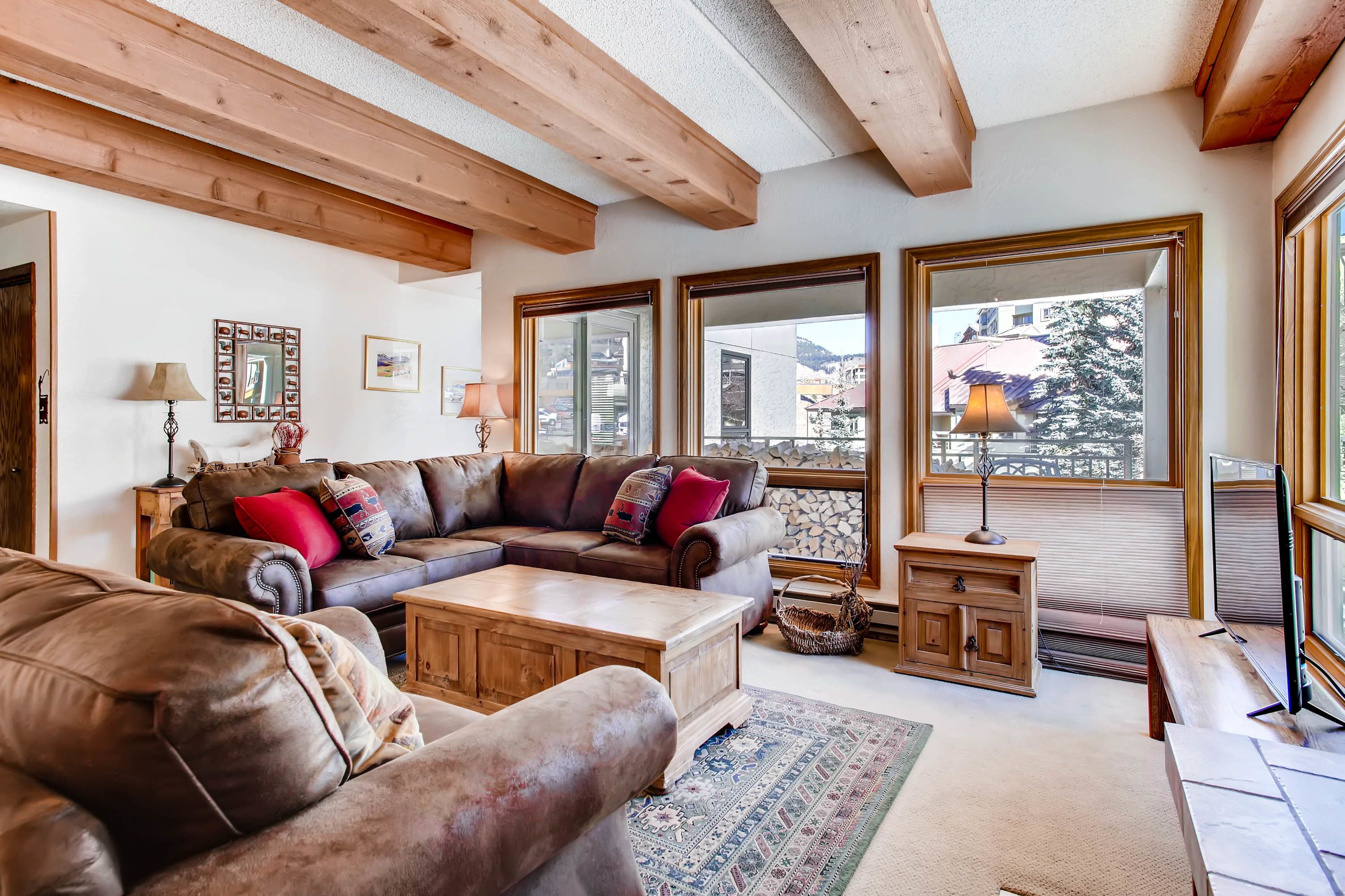 A cozy living room with a sectional sofa, a wooden coffee table, and large windows offering a view of the outside.