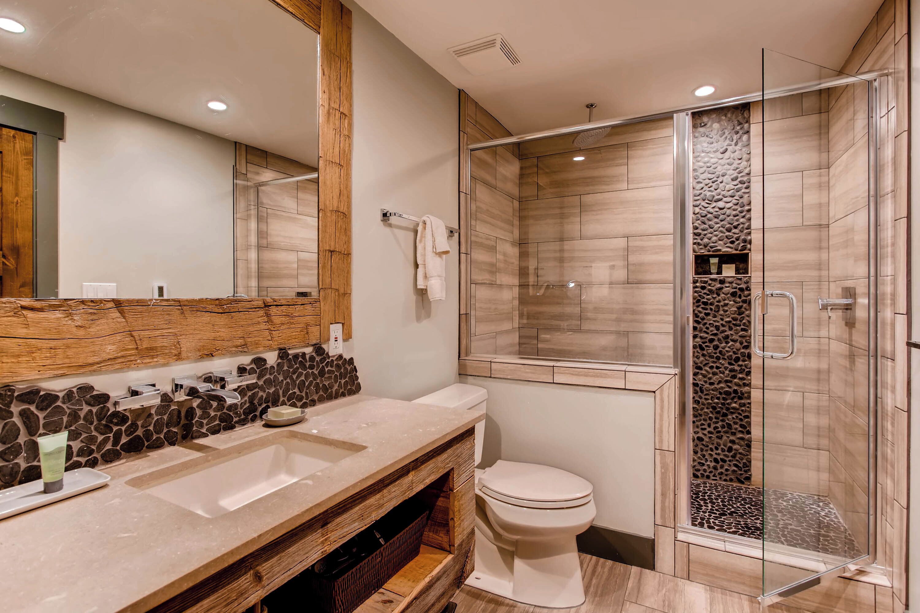 Une salle de bain moderne avec un meuble-lavabo en bois, deux vasques, des toilettes et une douche à parois de verre.
