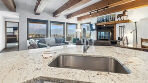 A modern kitchen with a large granite countertop, stainless steel sink, and wooden beams on the ceiling.