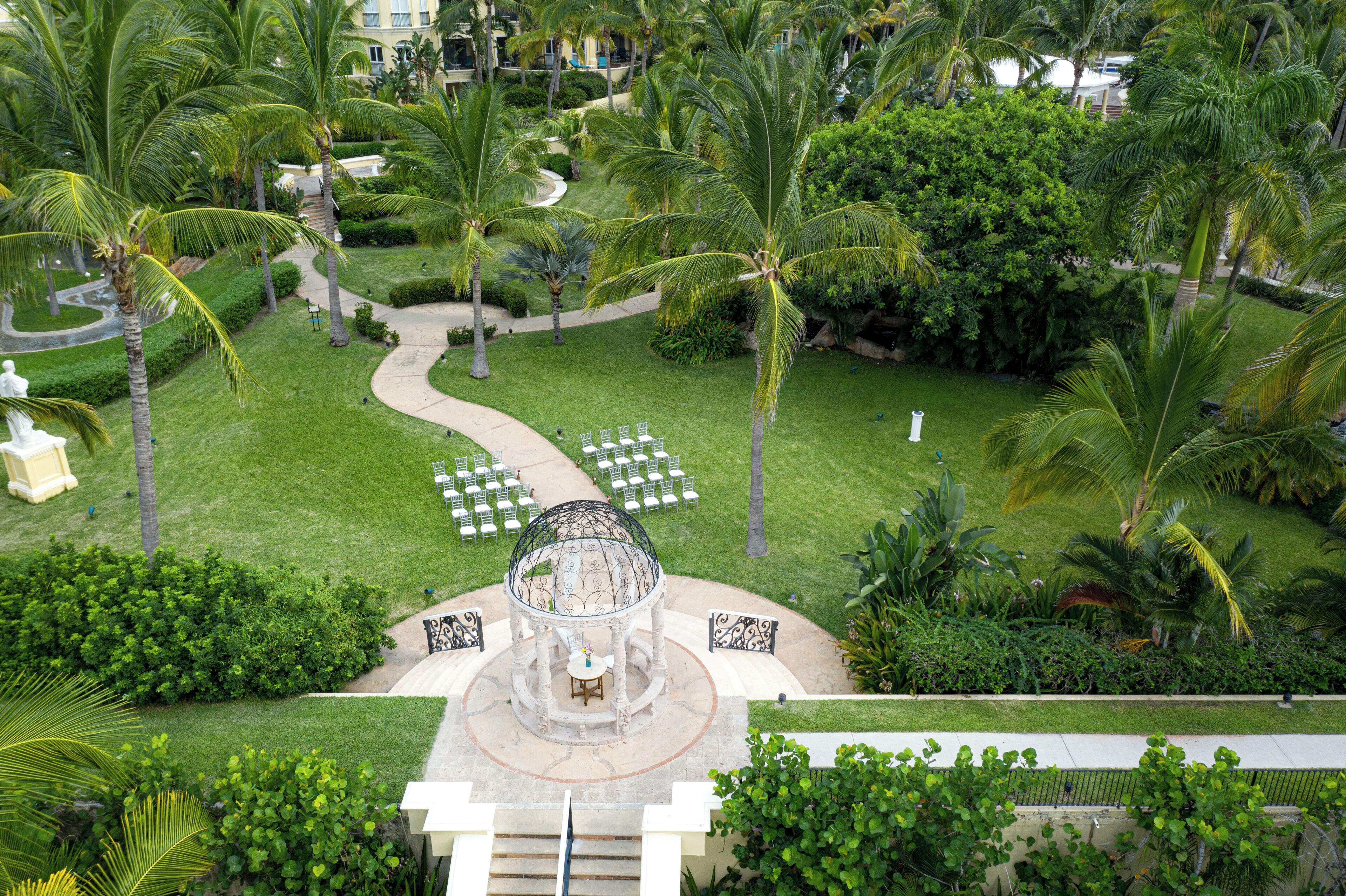 A lush garden with a central gazebo, surrounded by palm trees and a winding pathway.