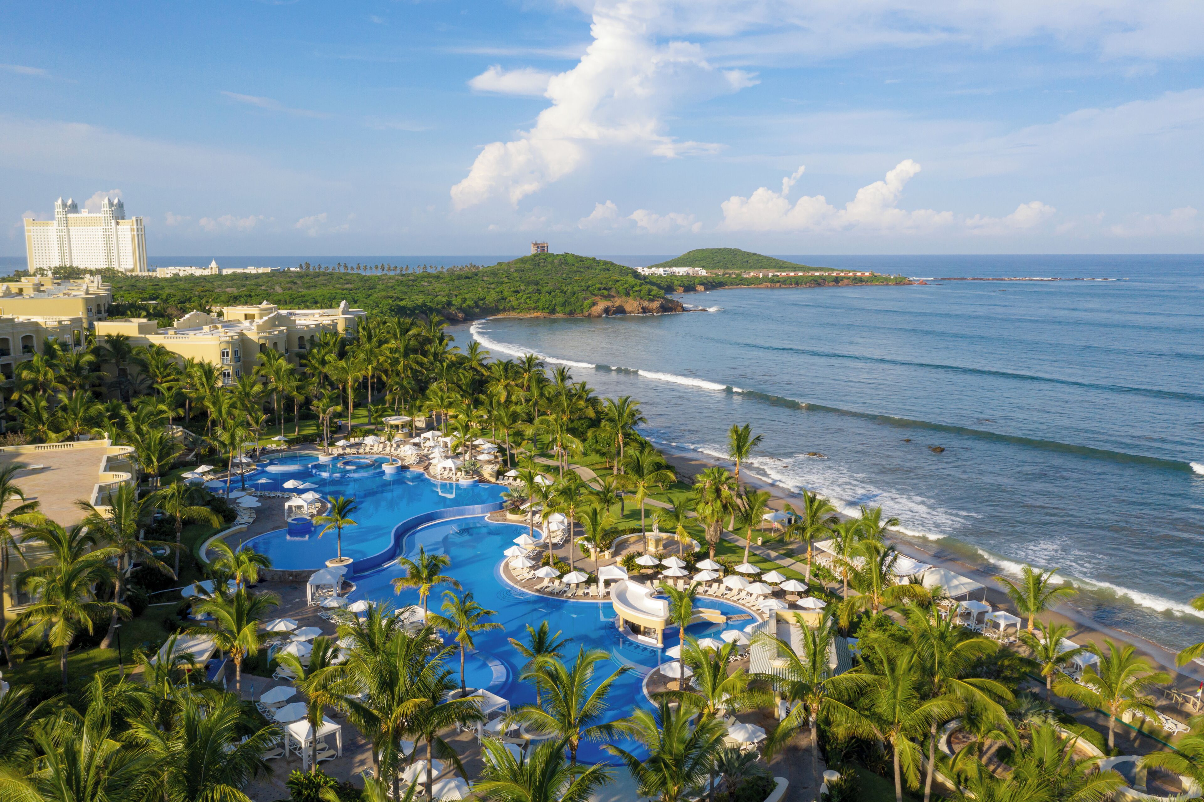 A resort with a large swimming pool, beachside lounge areas, and a view of the ocean.