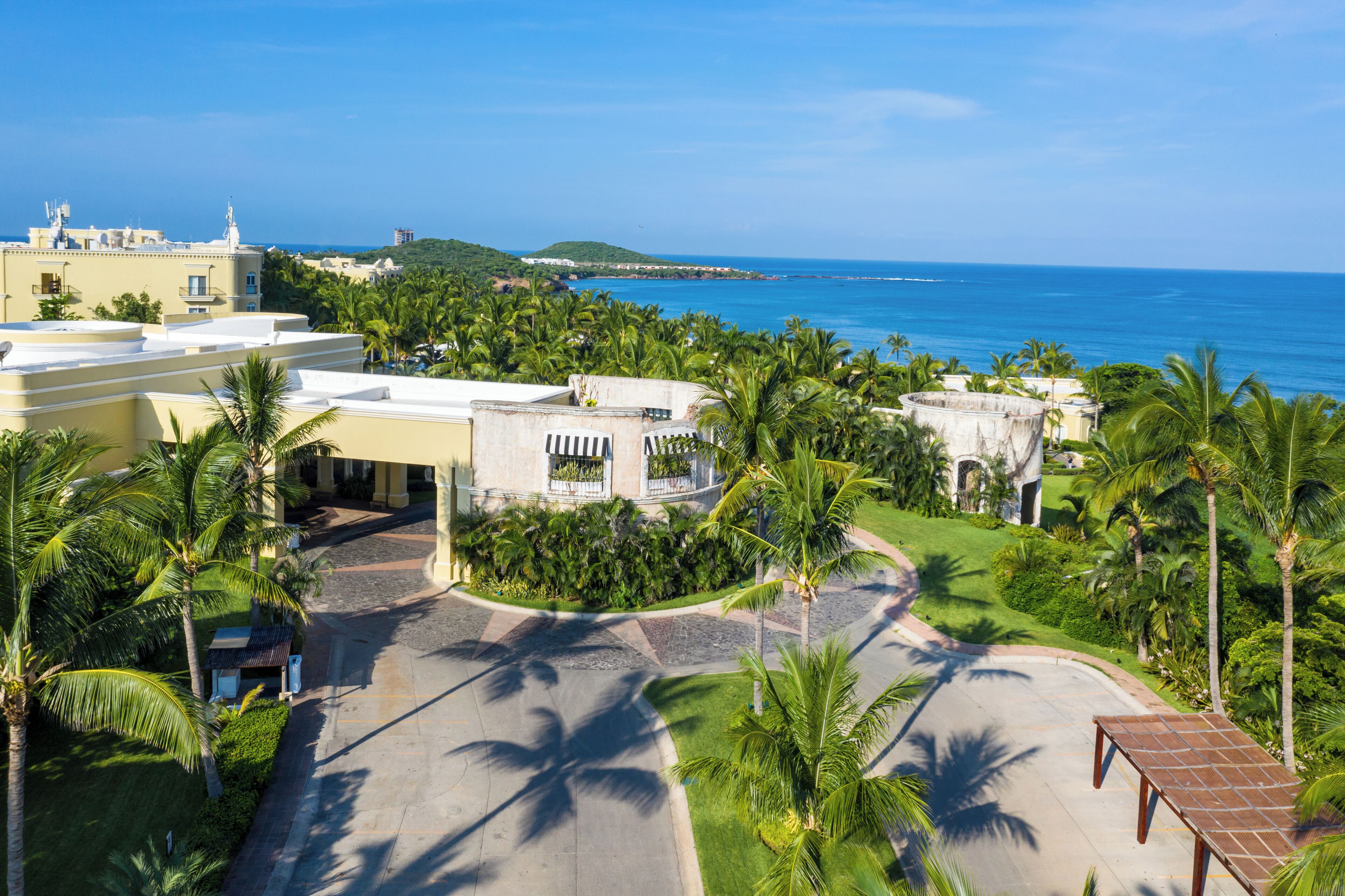 A resort with a paved driveway, palm trees, and a view of the ocean.