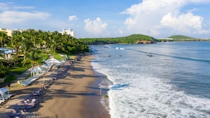 Uma praia com cadeiras de praia brancas e guarda-sóis, um edifício semelhante a um castelo e vista para o mar.