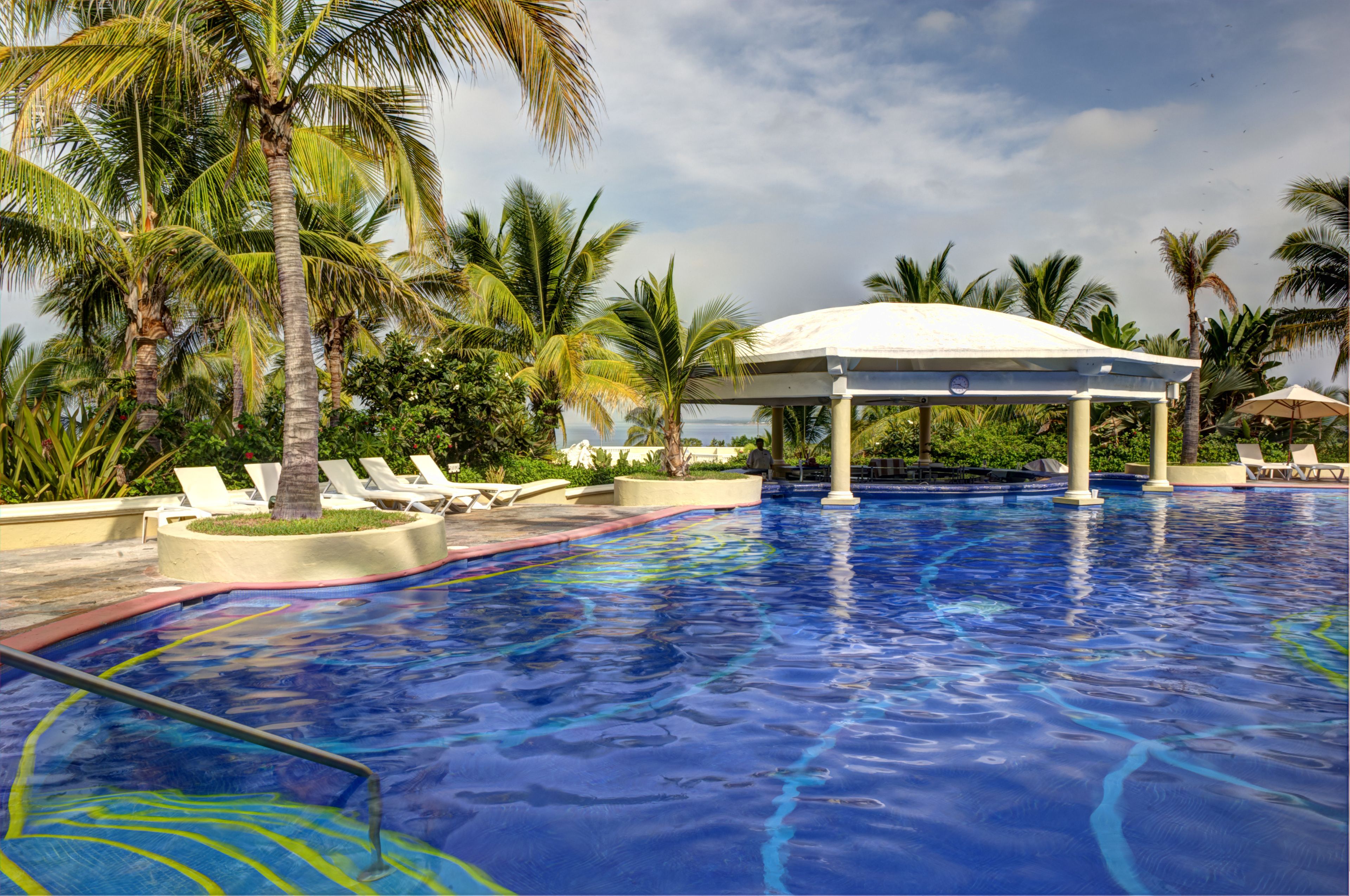 A swimming pool with lounge chairs and palm trees.