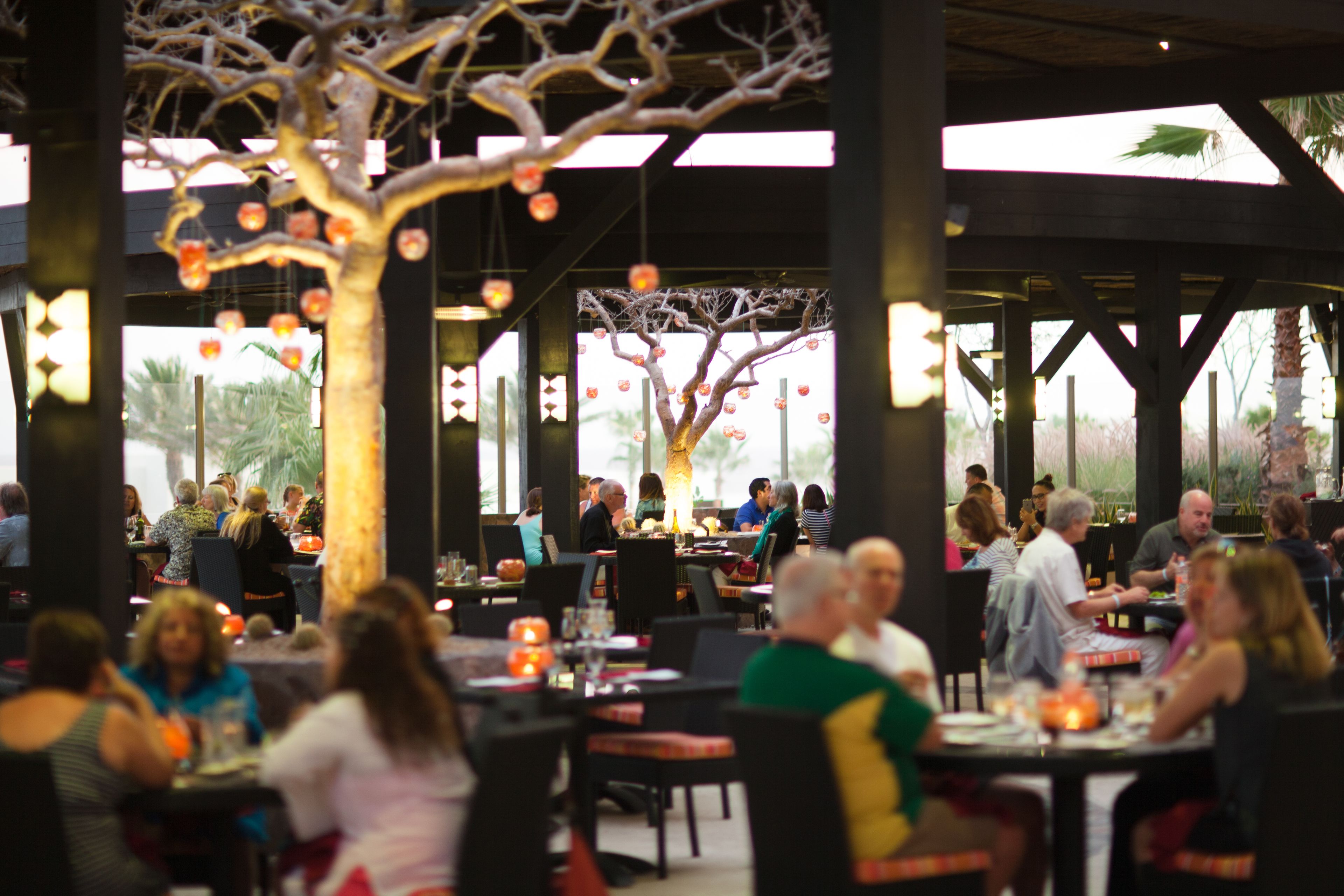 A restaurant with outdoor seating, covered by a roof, and decorated with hanging ornaments.