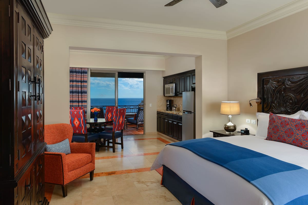 Habitación de hotel con cama, escritorio, silla, vista al océano y balcón.