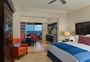 Habitación de hotel con cama, escritorio, silla, vista al océano y balcón.