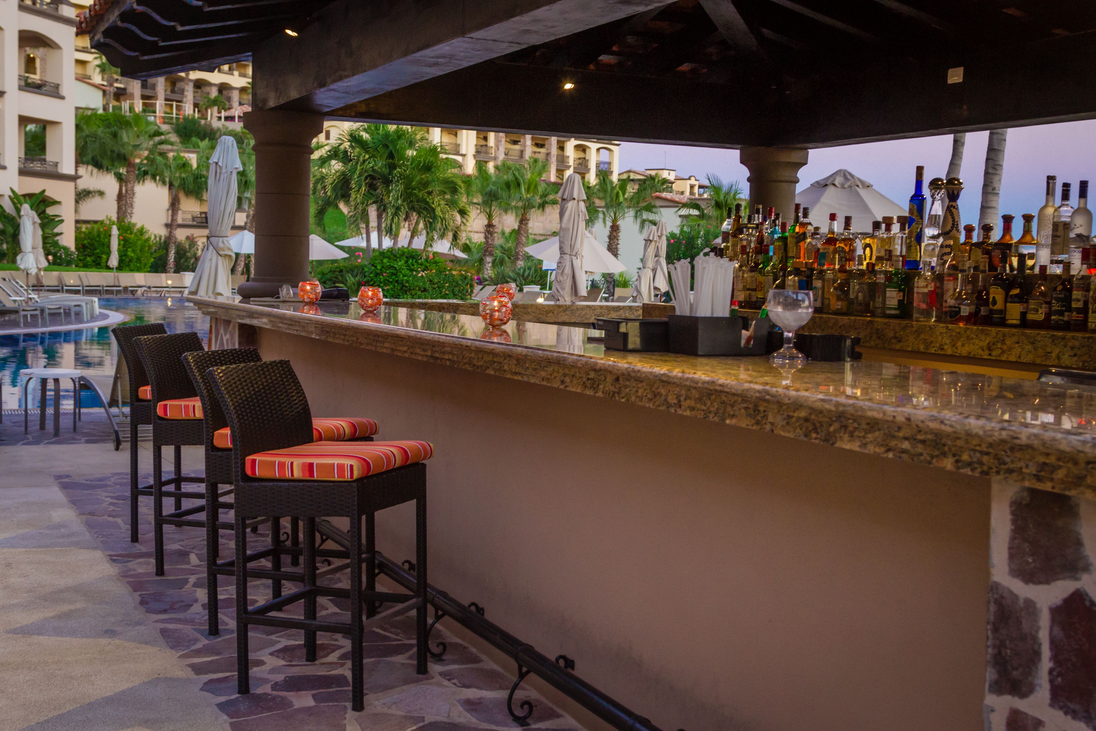Eine Bar mit Blick auf den Pool, mit Barhocker und einer Auswahl an Flaschen.