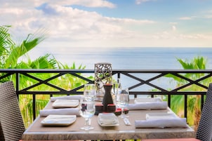 Mesa dispuesta para comer con vista al mar, rodeada de follaje.