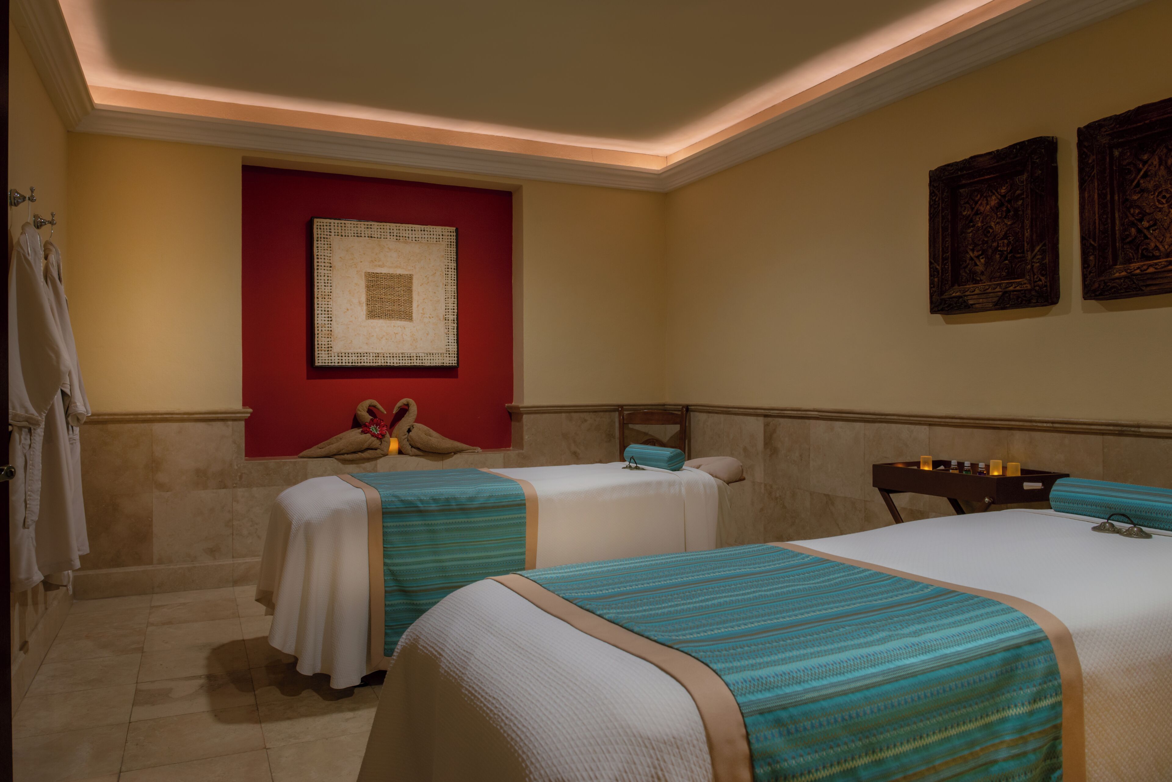 A hotel room with two beds, a red accent wall, and artwork.