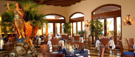 A restaurant with tables set for dining, a statue, and arched windows.