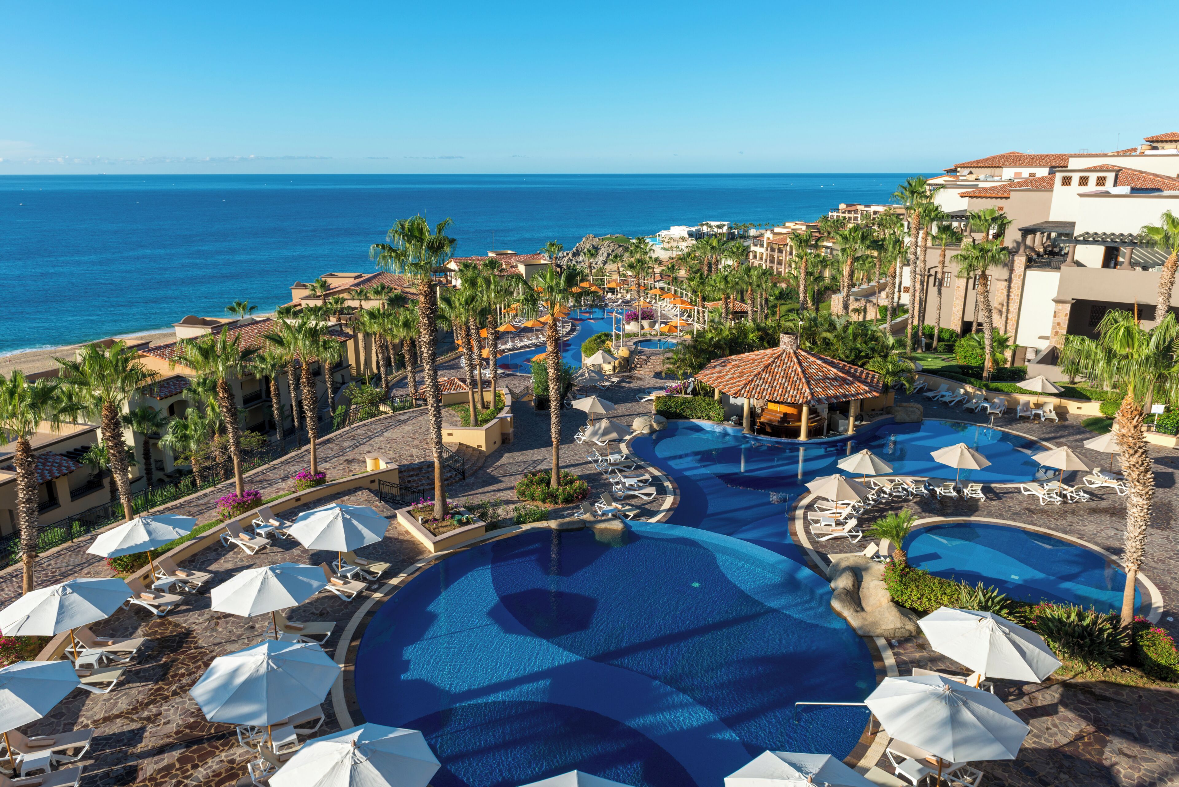 A resort with multiple swimming pools, palm trees, and a view of the ocean.