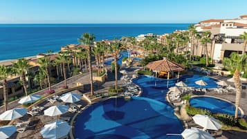 A resort with multiple swimming pools, palm trees, and a view of the ocean.