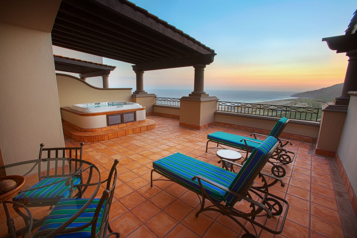 Una terraza con hidromasaje, sillones de descanso y vistas a la playa al atardecer.