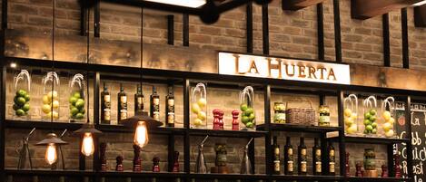 A bar area with shelves of bottles and glasses, a sign reading "LA HUERTA", and a brick wall background.