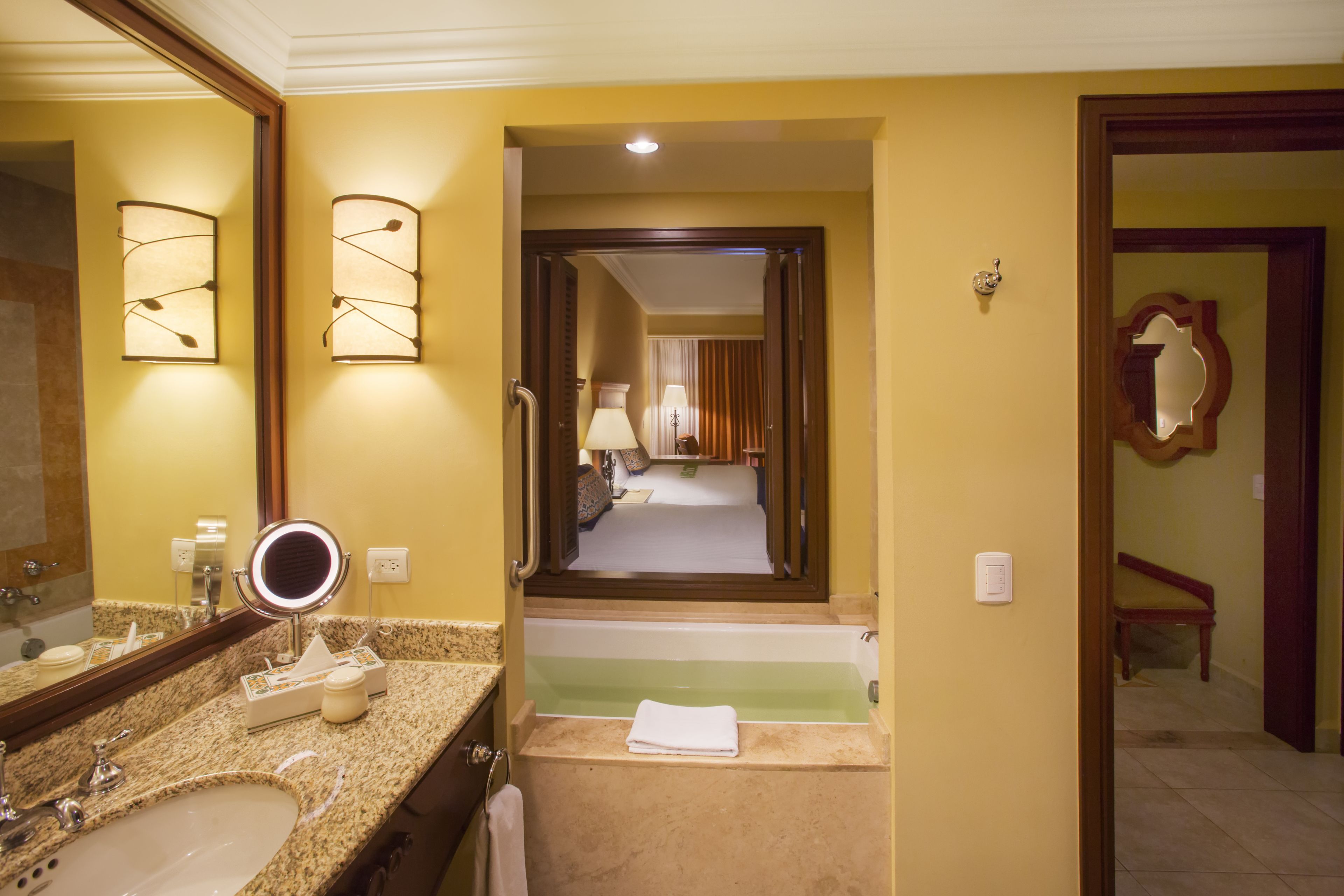 Ein Hotelbad mit einer Granittheke, einem Waschbecken, einem Spiegel, einer Badewanne und einer Tür zum Schlafzimmer.