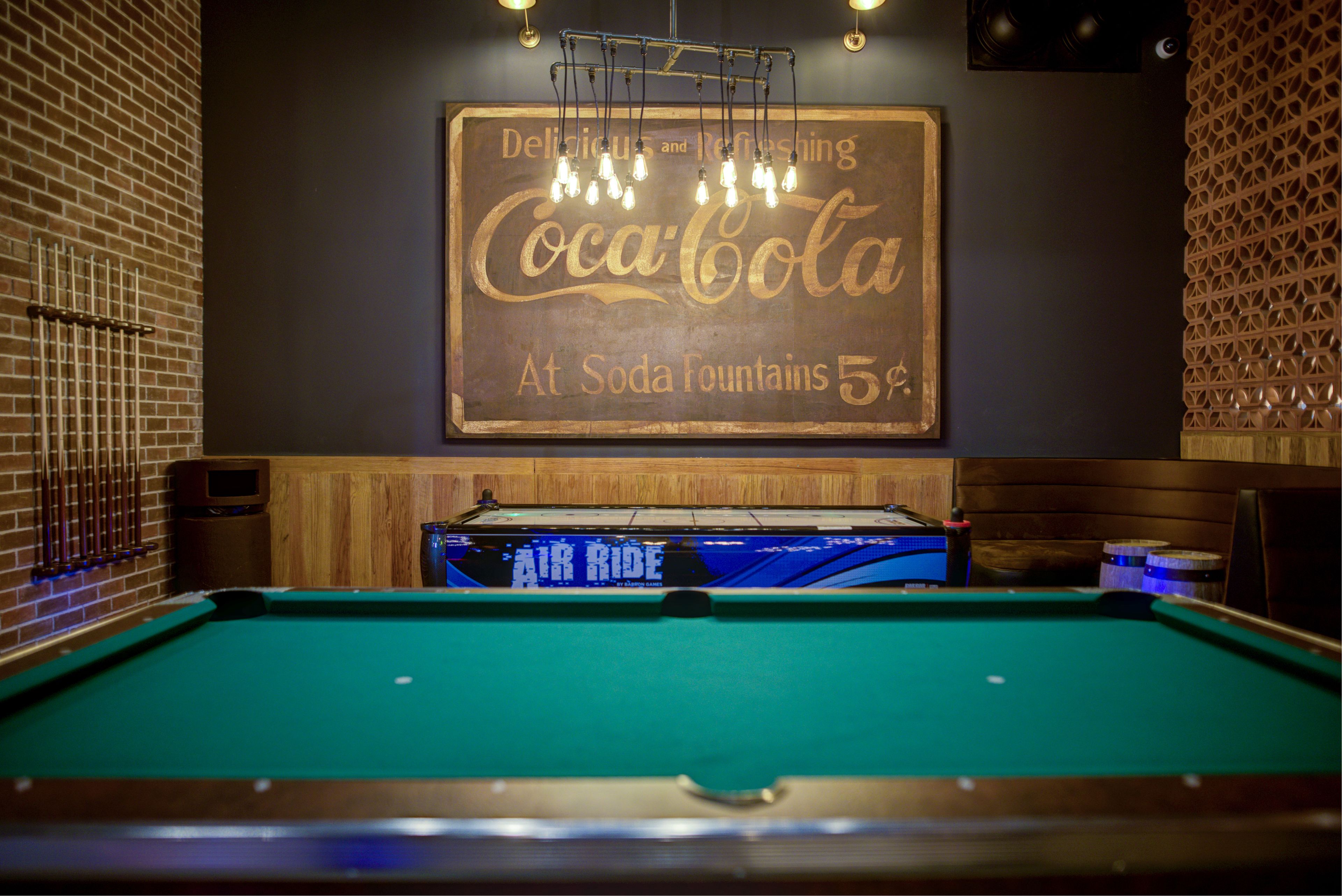 A billiards table with a Coca-Cola sign above it.