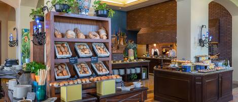 Un bufé de desayuno con panes y pastelería variados, una estación de café y una isla central con postres.