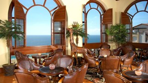 A seaside restaurant with wooden furniture, large arched windows, and a decorative horse statue. - Pueblo Bonito Sunset Beach Golf & Spa Resort - All Inclusive (Cabo San Lucas)