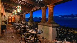 An outdoor dining area with stone flooring and metal chairs, featuring a view of the ocean at dusk. - Pueblo Bonito Sunset Beach Golf & Spa Resort - All Inclusive (Cabo San Lucas)