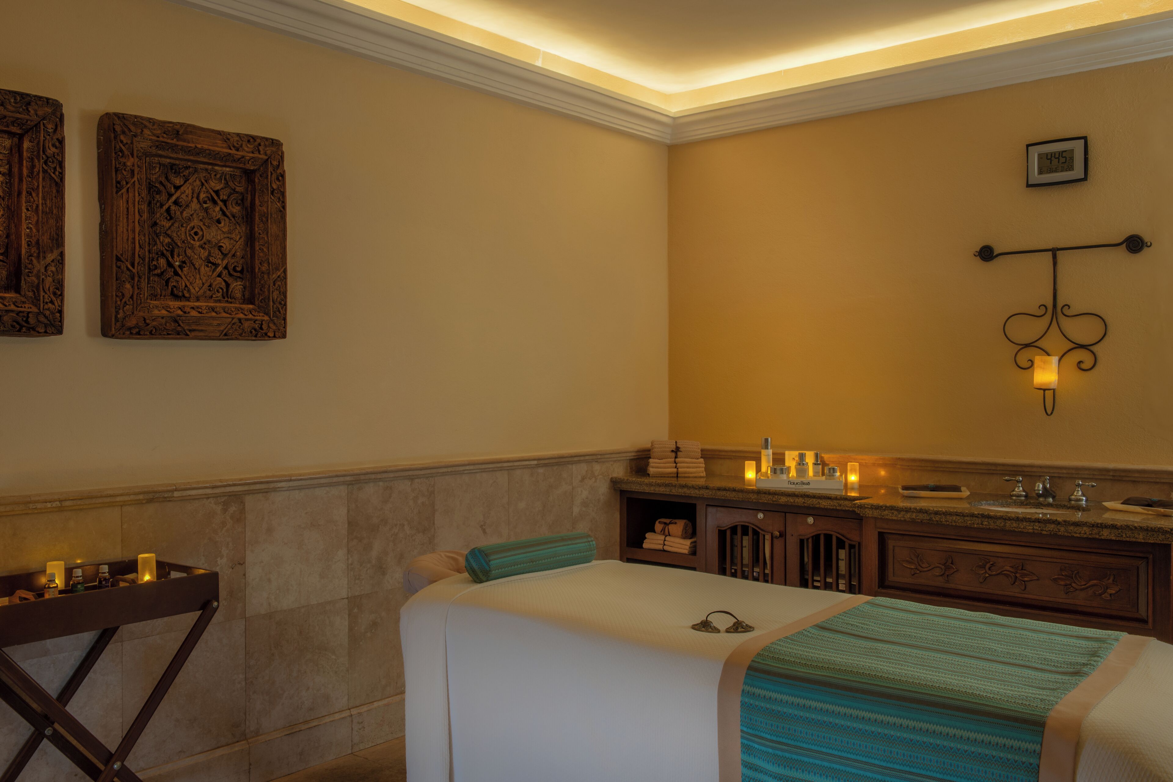 A hotel room with a bed, a vanity with a mirror, and a wall-mounted clock.