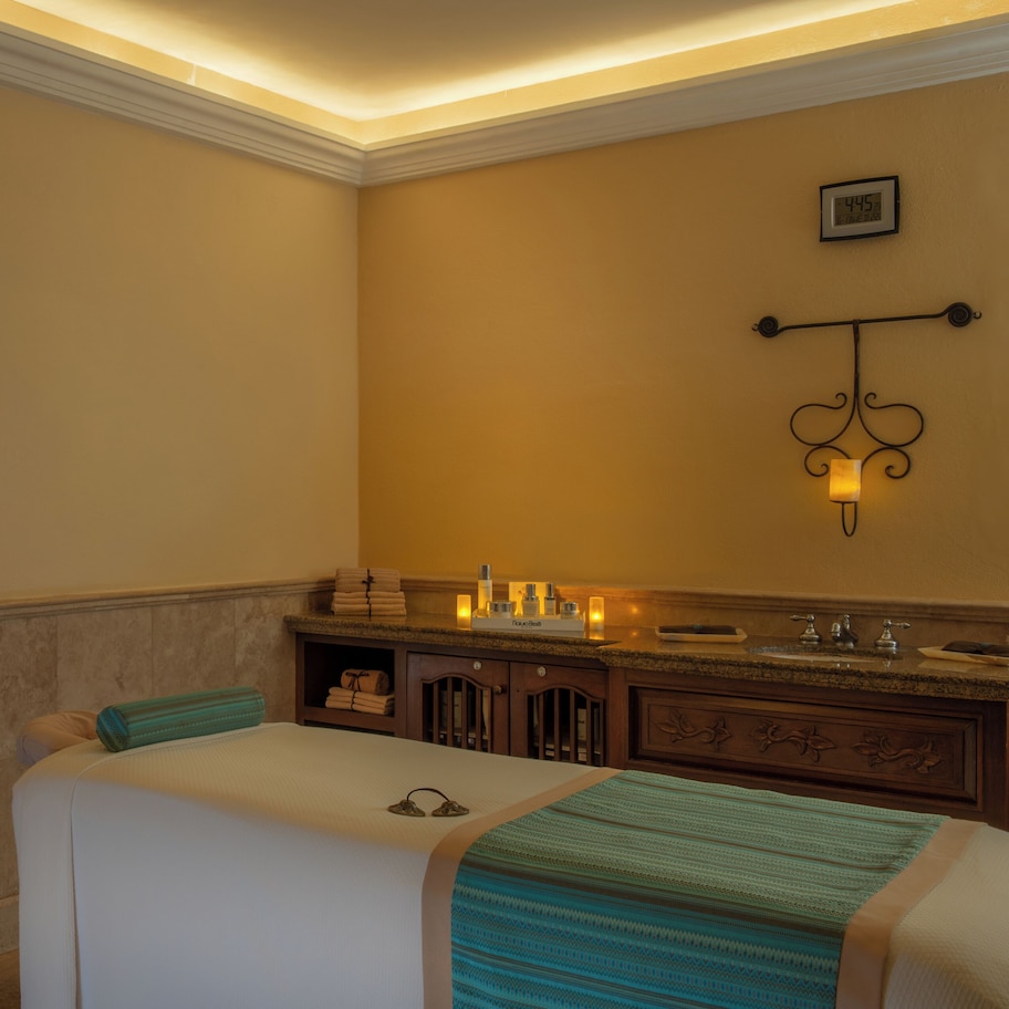 A hotel room with a bed, a vanity with a mirror, and a wall-mounted clock.