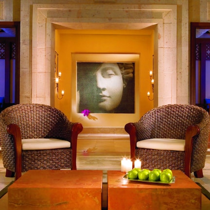 A lobby with two wicker armchairs facing each other, a table with green apples, and a painting above the chairs.