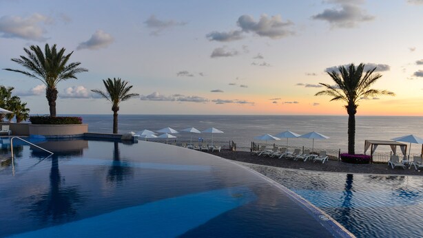 A poolside area with a view of the ocean at sunset, palm trees, and lounge chairs. - Pueblo Bonito Sunset Beach Golf & Spa Resort - All Inclusive (Cabo San Lucas)
