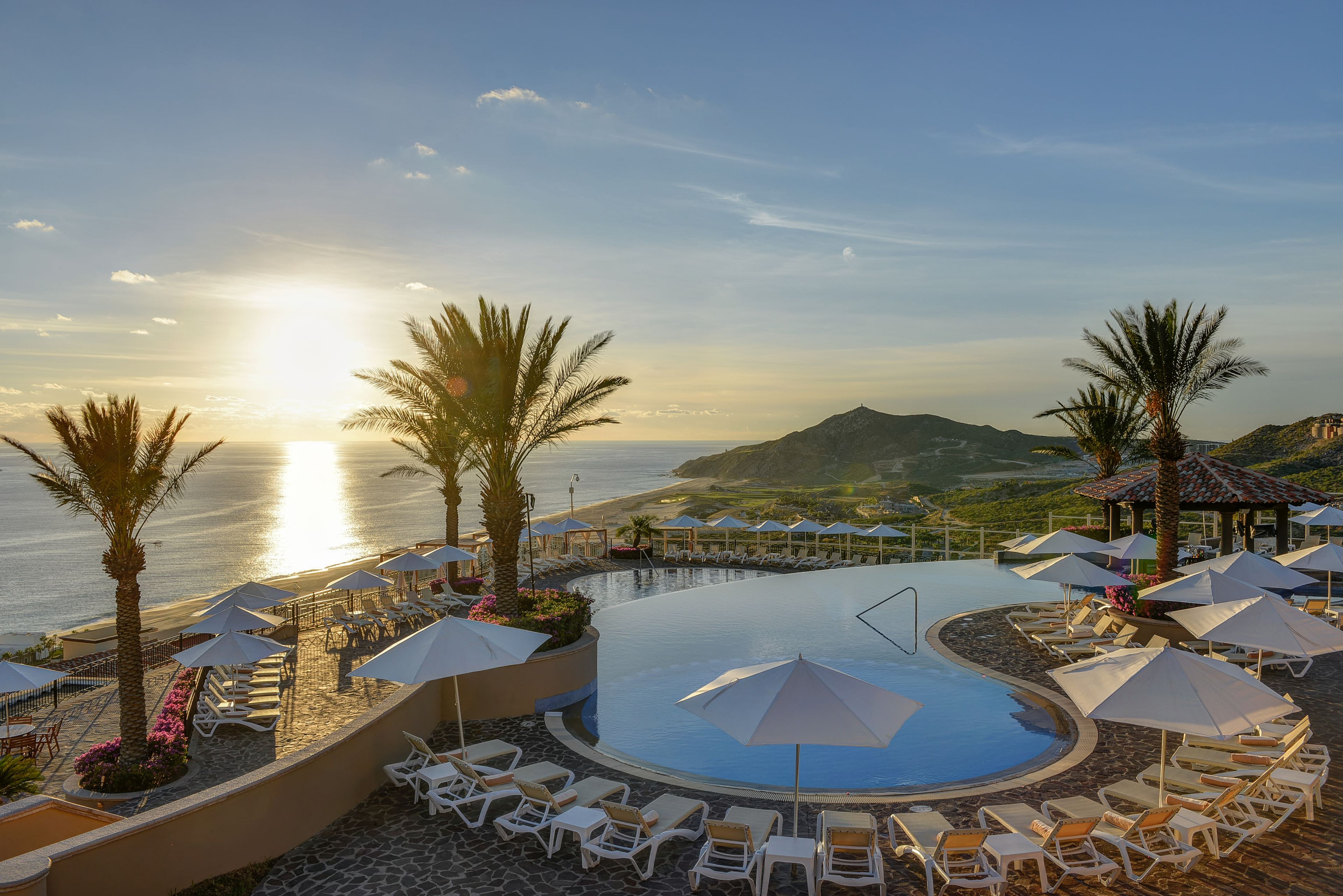 Ein Pool mit Liegestühlen und Sonnenschirmen mit Blick auf das Meer und einen Berg.