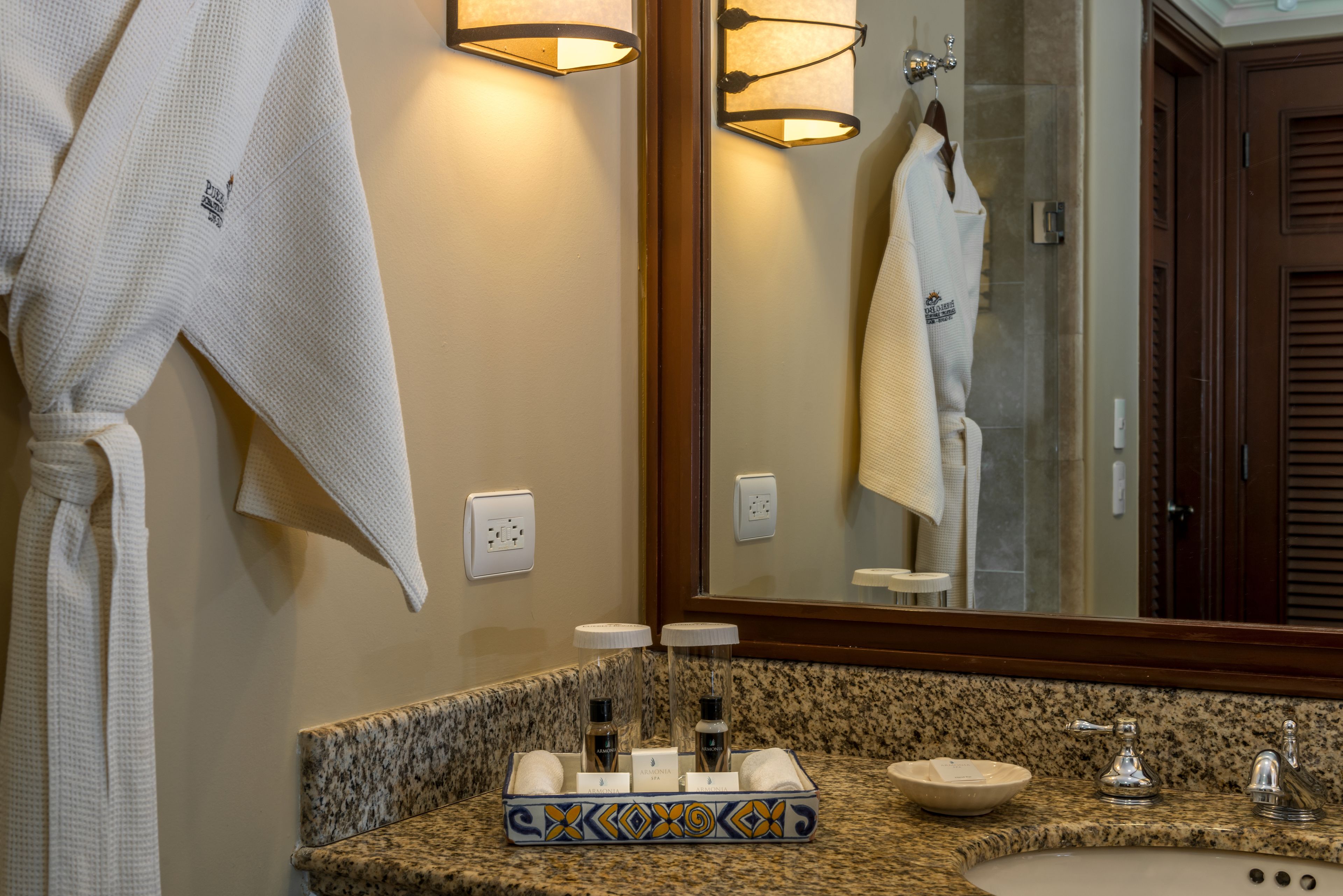 Une salle de bain avec un comptoir en granit, un lavabo, un miroir et deux peignoirs accrochés au mur.
