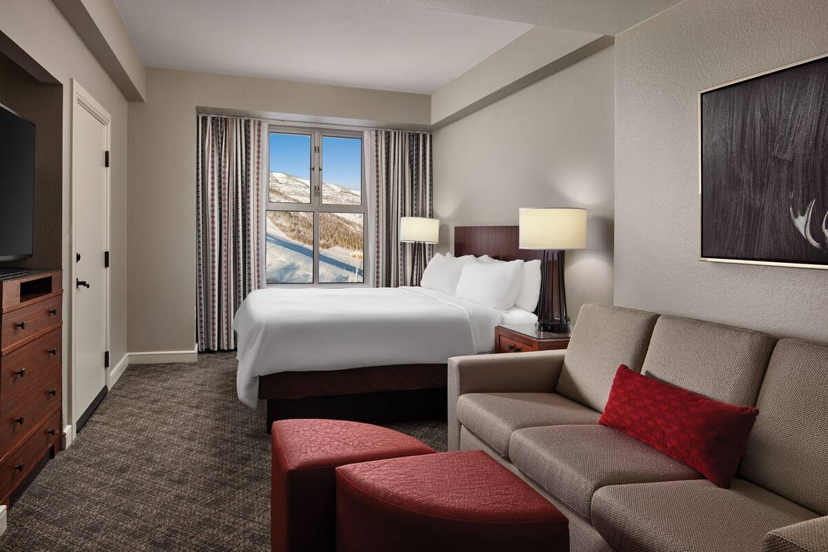 A hotel room with a large bed, a sofa, a TV, and a window with curtains.