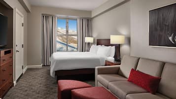 Una habitación de hotel con una cama grande, un sofá, un televisor y una ventana con cortinas.