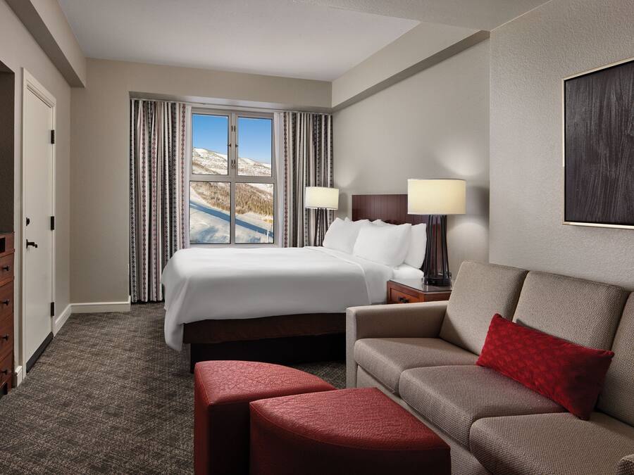A hotel room with a large bed, a sofa, a TV, and a window with curtains.
