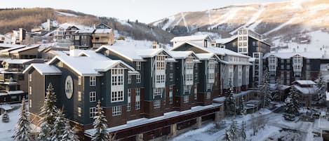 A multi-story hotel with a central atrium, surrounded by snow-covered trees and a mountainous backdrop.