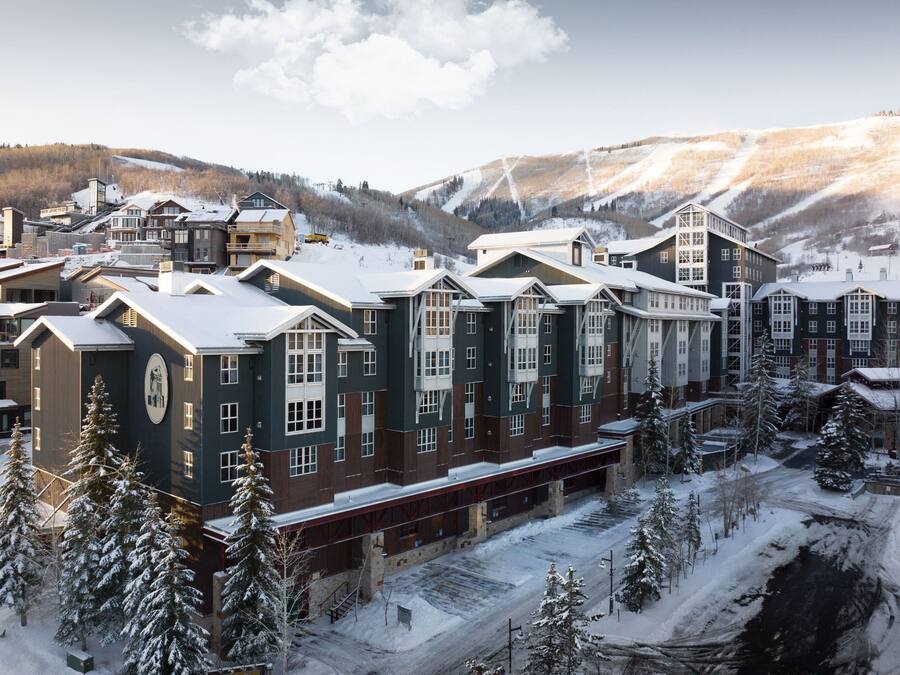 A multi-story hotel with a central atrium, surrounded by snow-covered trees and a mountainous backdrop.