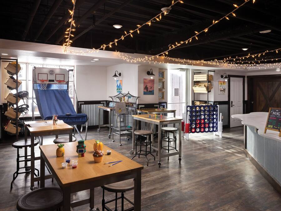 A modern interior with a wooden table, chairs, and string lights. There are shelves with items and a counter with a sign.