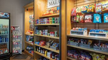 Een gangpad in een supermarkt met schappen vol snacks, drankjes en huishoudartikelen.
