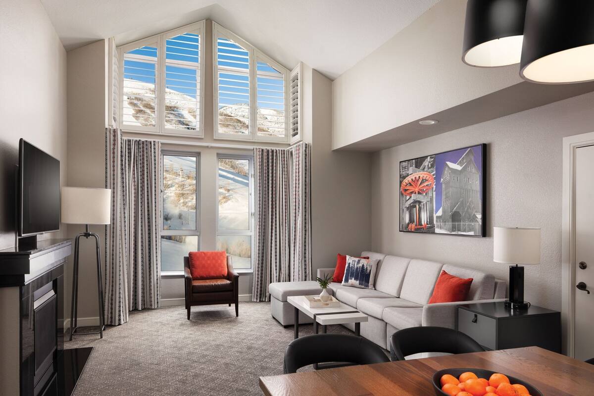 A modern living room with a large window, a flat-screen TV, a sofa, a dining table, and a coffee table.